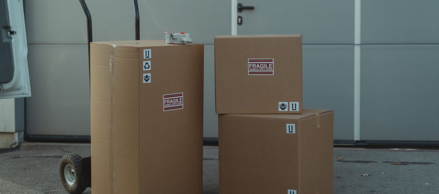 Three cardboard boxes on a dolly, ready for shipping outside a warehouse.