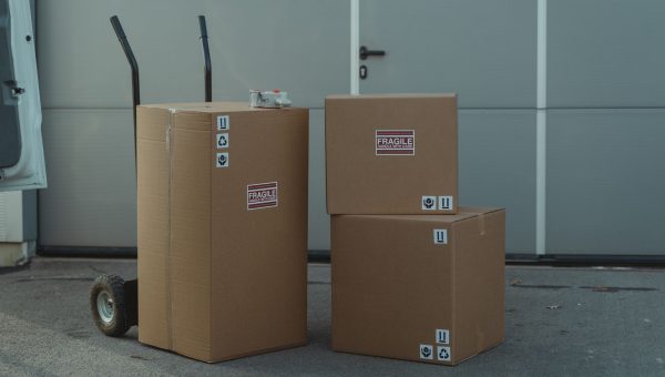 Three cardboard boxes on a dolly, ready for shipping outside a warehouse.