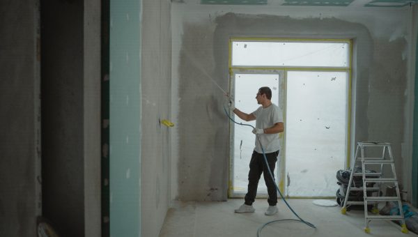 A man sprays paint on a wall while renovating an indoor room with professional equipment.
