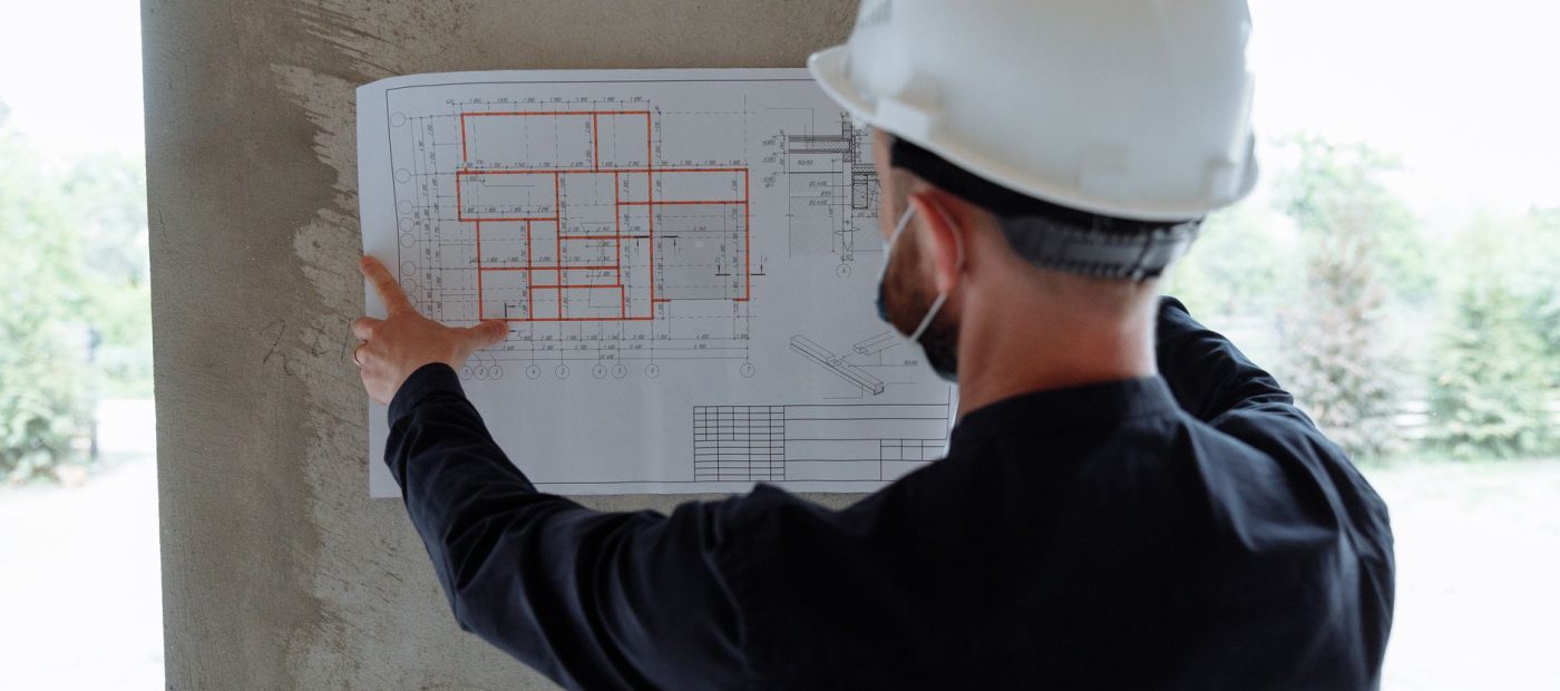 Engineer in hardhat reviewing architectural floor plans at construction site.